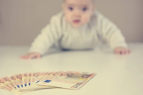 Baby schaut auf Geldhaufen auf einem Tisch. — Stockfoto