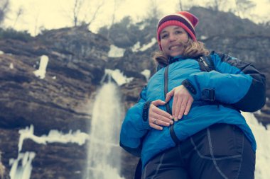 Aktif genç hamile kadının karnı üzerinde bir kalp oluşturan.