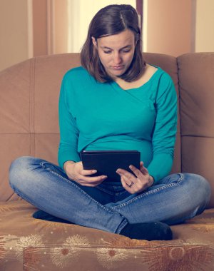 Hamile kadın bir tablet bir kanepede okuma.