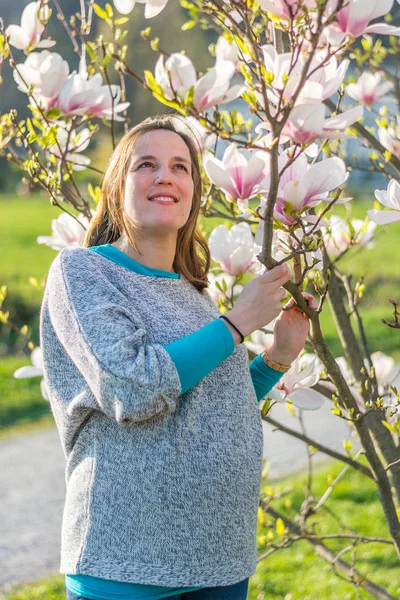 Wanita hamil berpose dengan mekar pohon magnolia . — Stok Foto