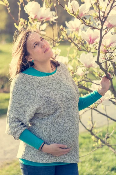 Wanita hamil berpose dengan mekar pohon magnolia . — Stok Foto
