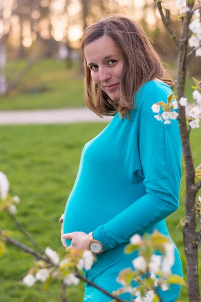 Attractive young mother posing by blooming cherry tree. — Stock Photo, Image