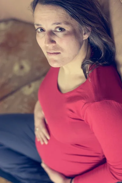 Anne giyen kırmızı gömlek casualy bir kanepede oturan bekliyor. — Stok fotoğraf