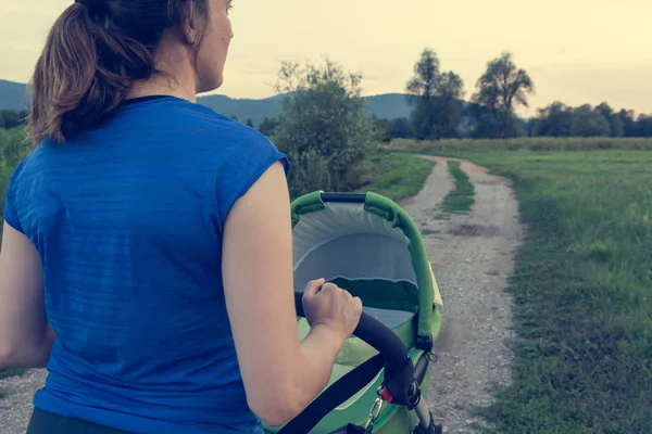 Mãe ativa empurrando um carrinho ao pôr do sol . — Fotografia de Stock