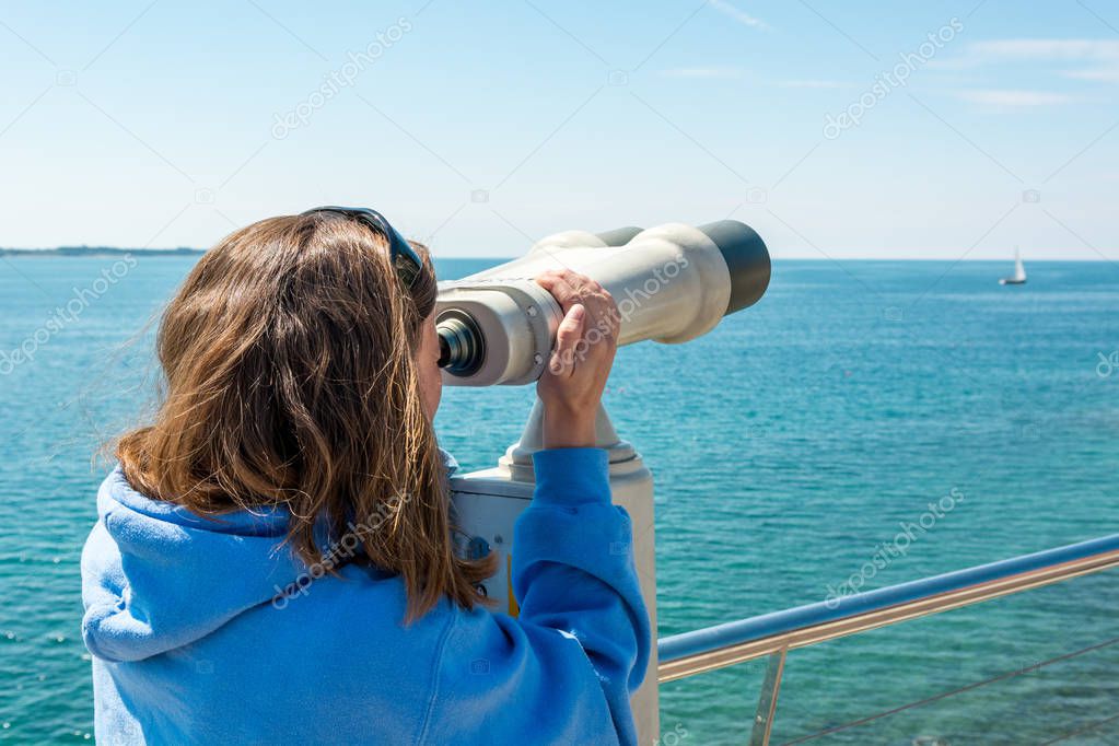 Woman looking through coin operated binoculars at seaside.