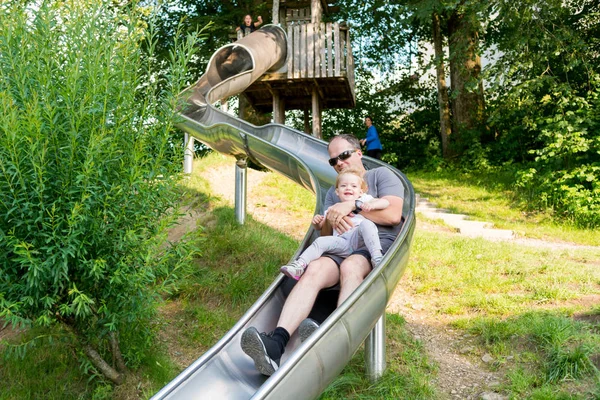 Father and daughter riding a long slide at local park.