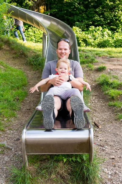 Father and daughter riding a long slide at local park.