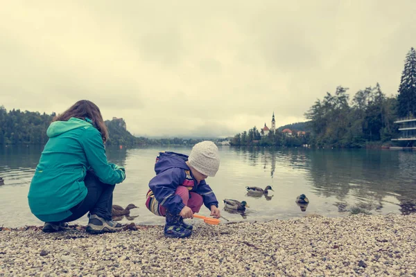 Mutter und Tochter spielen am Seeufer mit romantischer Kirche im Speck. — Stockfoto