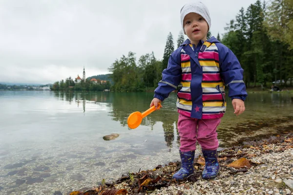 Linda chica jugando en la orilla del lago con pala de plástico . — Foto de Stock