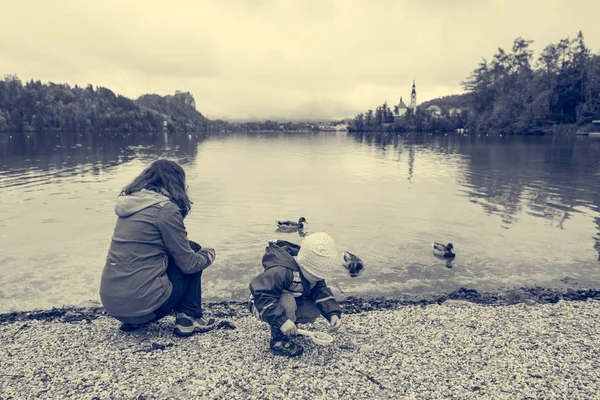 Mãe e filha brincando na margem do lago com igreja romântica no bacground . — Fotografia de Stock