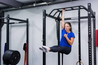 Aktif esmer kız barfiks aletinde tek elle bacak kaldırarak eğleniyor..