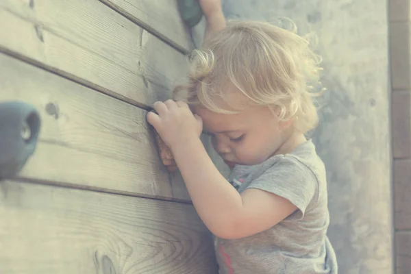 Portrait of cute blonde girl climbing plastic boulder wall outdoor.