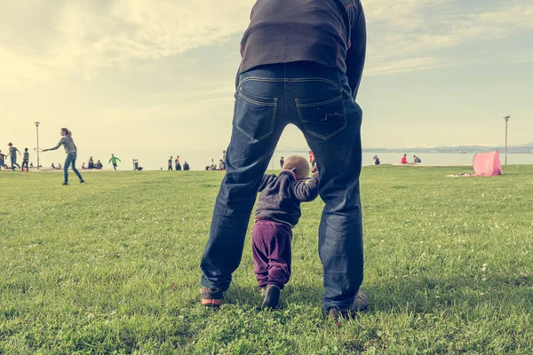Mignon bébé fille apprendre à marcher avec son père dans un parc . — Photo