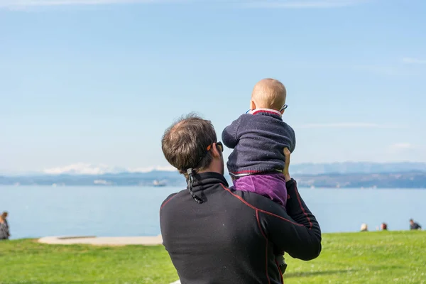 Visão traseira de um pai segurando sua filha bebê bonito e olhando para o mar . — Fotografia de Stock