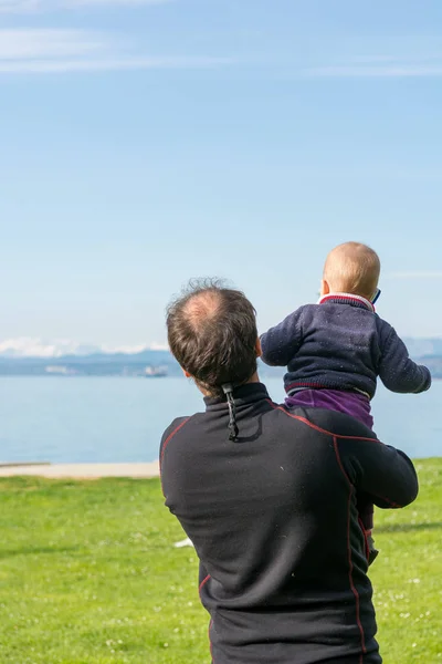 Visão traseira de um pai segurando sua filha bebê bonito e olhando para o mar . — Fotografia de Stock