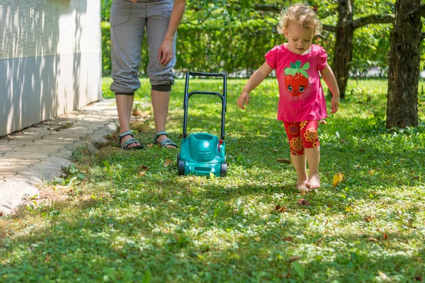 Cute girl lawn mowing with plastic toy mower.