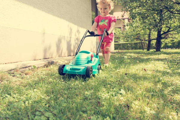 Cute girl koszenie trawnika z plastikowej kosiarki zabawki. Obraz Stockowy