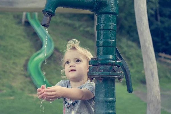 Menina loira bonito lavar as mãos usando bomba de água mão no parque local . — Fotografia de Stock