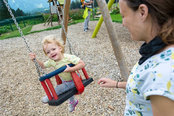 Mãe empurrando sua filha em um balanço no parque infantil ao ar livre . — Fotografia de Stock