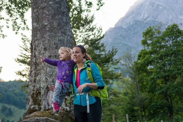 Mother supporting her daughter standing on tree trunk exploring the forest view in mountains. — ストック写真