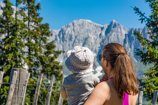 Mãe segurando sua filha no colo apreciando a vista da montanha e mostrando a paisagem . — Fotografia de Stock