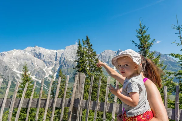 Mor håller sin dotter i knä njuter av bergsutsikten och visar landskapet. — Stockfoto