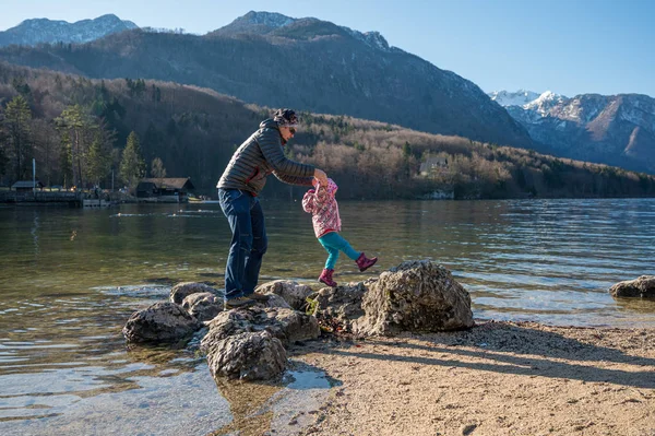 Menina bonito e pai andando através de pedras no lago . — Fotografia de Stock