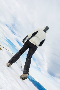 Karla kaplı dağ sırtında yürüyen kişinin alçak açılı görüntüsü.