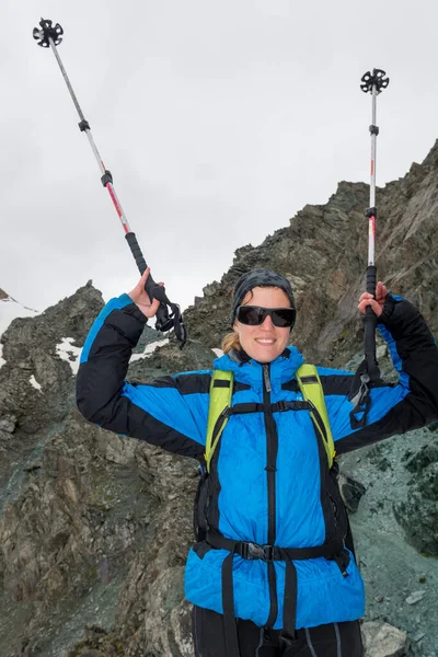 Female mountaineer celebrating ascend with walking poles raised high. — Stock Photo, Image