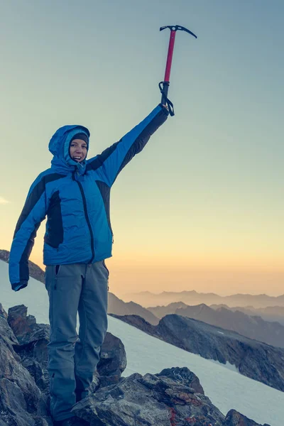 Kvinnlig bergsklättrare firar framgångsrik uppstigning med is yxa upp i skyn. — Stockfoto