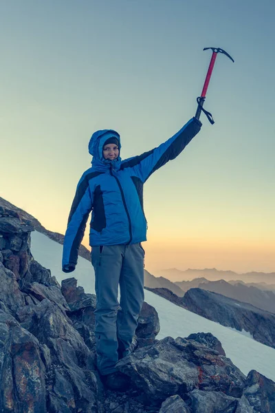 Female mountaineer celebrating successfull ascend with ice axe raised into the sky. — Stock Photo, Image