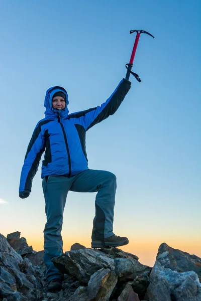 Mujer montañista celebrando exitosa ascensión con hacha de hielo elevada al cielo . — Foto de Stock