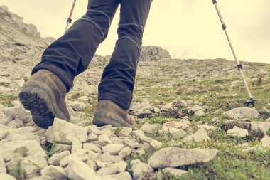 Düşük açılı bir bakış açısıyla kadın, baston kullanarak kayalık bir yamaçtan yükseliyor..
