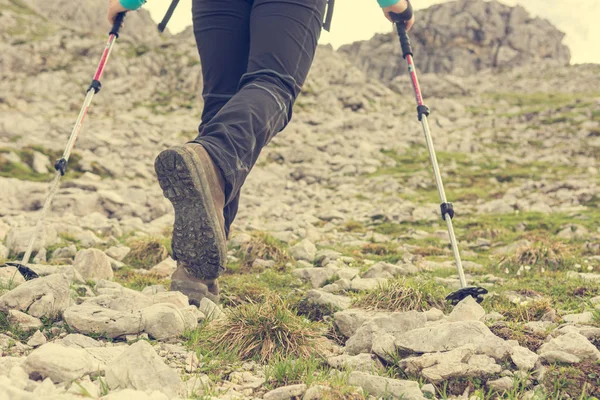 Low angle view of female ascending a rocky slope using walking poles.