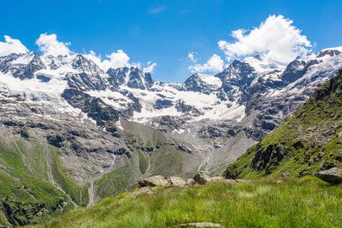 Zirveleri ve yamaçları yemyeşil vadide buzullarla kaplı muhteşem bir dağ manzarası..