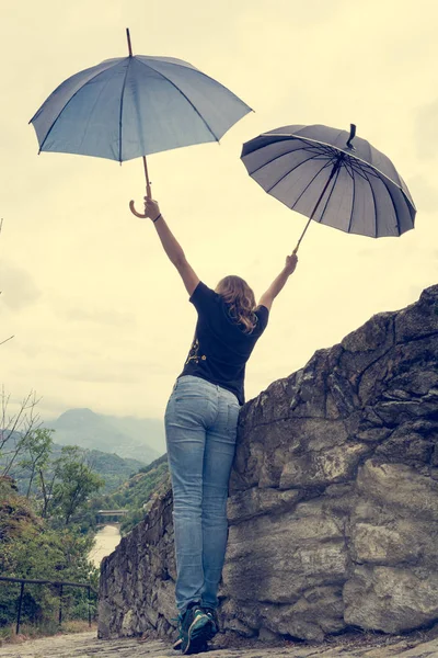 Young female dancing in the rain using pair of umbrellas.