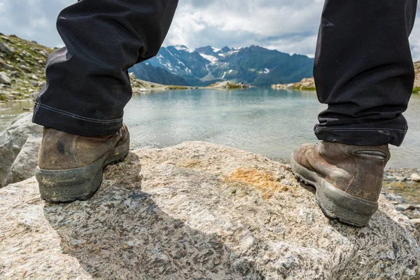 Low angle view of feet standing on a rock above mountain lake.