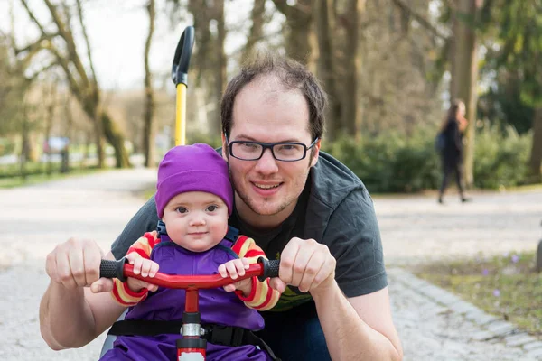 Niña y su padre posando en una bicicleta infantil en un parque . — Foto de Stock