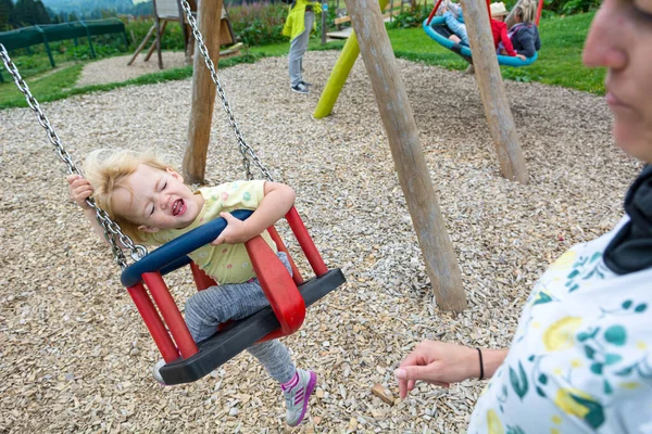 Mãe empurrando sua filha em um balanço no parque infantil ao ar livre . — Fotografia de Stock