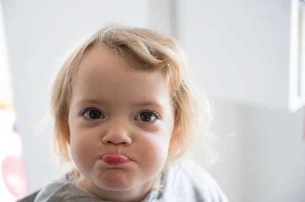 Porträtt av en söt blond flicka poserar i ett kök gör ansikten. — Stockfoto