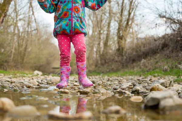 Młoda dziewczyna spaceruje po płytkim strumieniu w gumowych różowych butach. — Zdjęcie stockowe