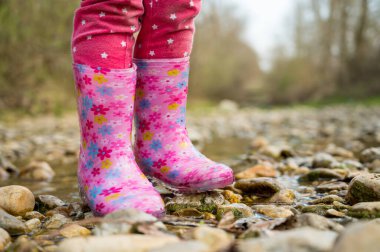 Lastik pembe çizmelerle sığ bir derede yürüyen genç kız..