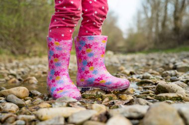 Lastik pembe çizmelerle sığ bir derede yürüyen genç kız..