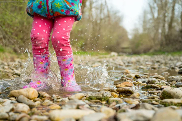 Giovane ragazza che cammina lungo un ruscello poco profondo con stivali di gomma rosa . — Foto Stock