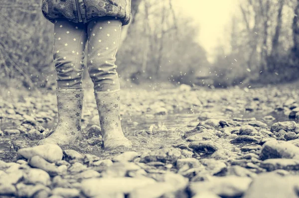 小女孩穿着橡胶粉色的靴子沿着一条浅浅的小河走着. — 图库照片