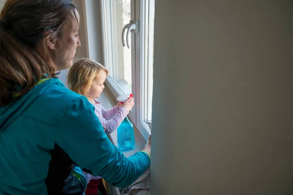 Söt flicka som hjälper mamma att rengöra fönster. — Stockfoto