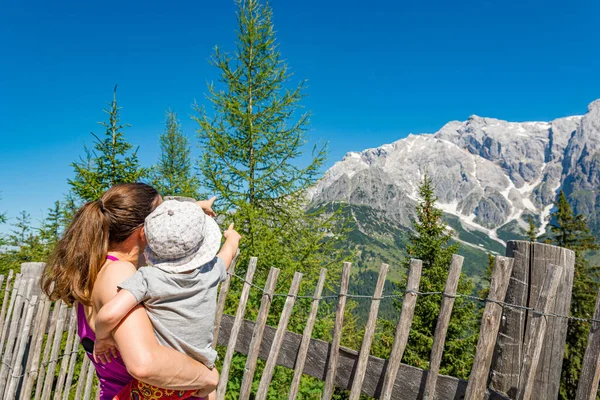 Mor håller sin dotter i knä njuter av bergsutsikten och visar landskapet. — Stockfoto