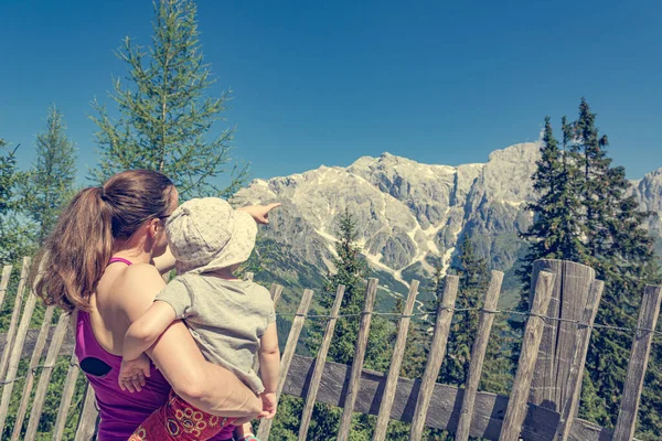 Mãe segurando sua filha no colo apreciando a vista da montanha e mostrando a paisagem . — Fotografia de Stock