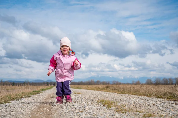 Nettes Mädchen in rosa Jacke springt auf Feldweg, der von Feldern umgeben ist. — Stockfoto
