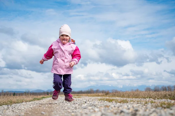 Menina bonito correndo ao longo estrada de terra cercada de campos . — Fotografia de Stock